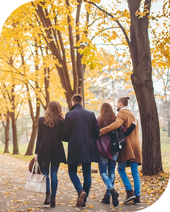 Group of four people walking down a path in the park, surrounded by trees with their leaves changing colors