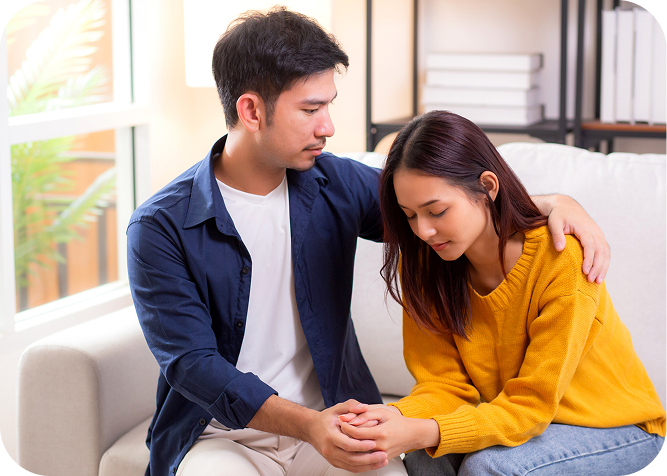 Man and woman sitting on a couch, holding hands, with a window
