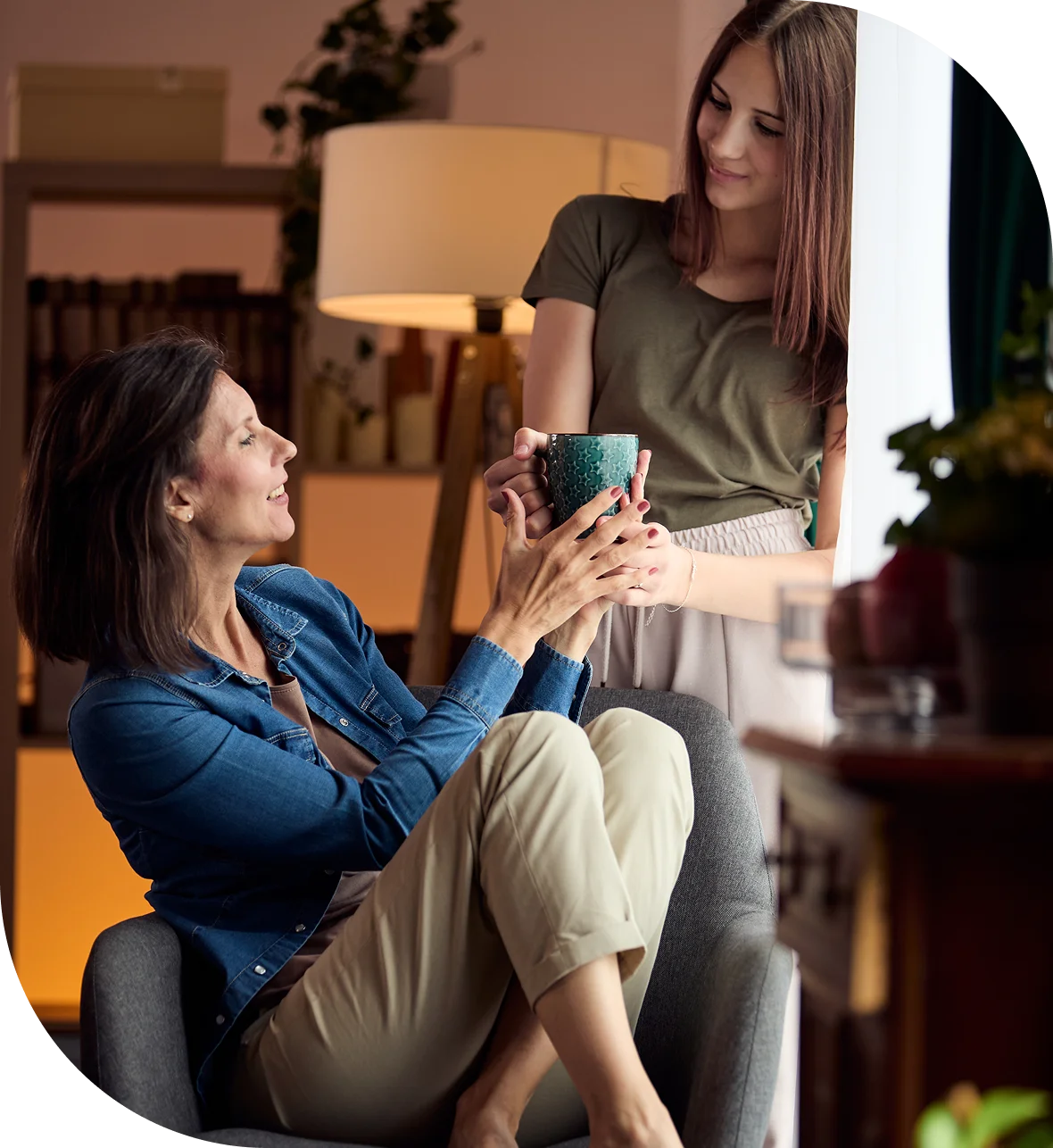 Two women sitting in a chair, one of them holding a cup of coffee